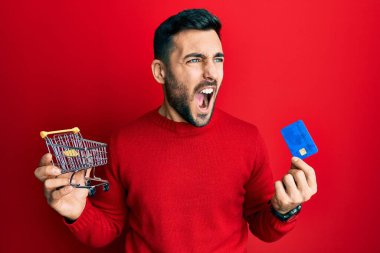 Genç İspanyol adam elinde küçük bir market arabası ve kredi kartı tutuyordu kızgın ve öfkeli çığlıklar atıyordu öfkeyle bağırıyordu. öfke ve agresif konsept. 