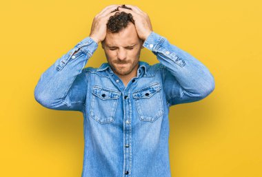 Sıradan kot ceket giyen genç İspanyol adam acı ve migren yüzünden çaresiz ve stresli baş ağrısı çekiyor. Eller başının üstünde.. 