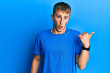 Gündelik mavi t-shirt giyen genç beyaz adam elini yana uzatarak şaşırdı, ağzı açık hayret içinde kaldı.. 