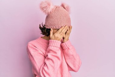 Genç esmer kadın, ağlarken yüzünü ellerle kapatan sevimli yün şapkalı. depresyon kavramı. 