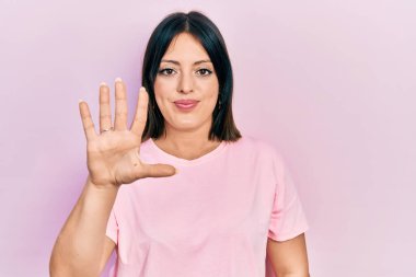 Gündelik pembe tişört giyen genç İspanyol kadın beş numarayı gösterip işaret ederken kendinden emin ve mutlu bir şekilde gülümsüyor.. 