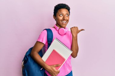 Okul çantası takan ve elinde kitaplarla gülümseyen, ağzı açık, gülümseyen Afro-Amerikalı genç bir kız. 