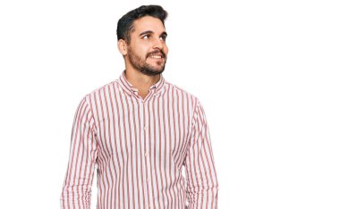 Genç İspanyol bir adam iş gömleği giyiyor. Yüzünde gülümseme ve doğal bir ifadeyle yan yana bakıyor. Kendinden emin gülen. 