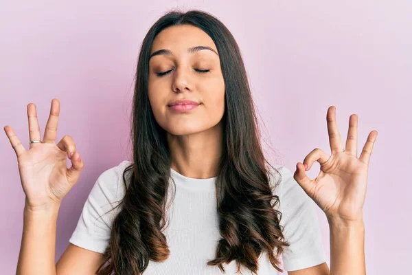 カジュアルな白いTシャツを着た若いヒスパニック系の女性がリラックスし 指で瞑想ジェスチャーを行う目を閉じて笑顔 ヨガのコンセプト — ストック写真