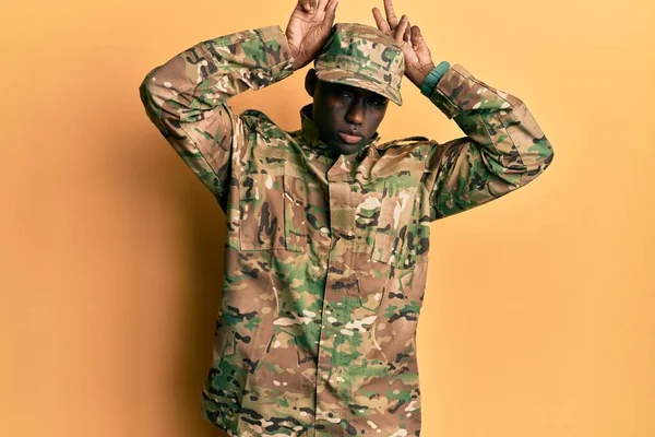 軍の制服を着た若いアフリカ系アメリカ人男性は 手のヤシの木とウサギの耳のジェスチャーを行うシニカルで懐疑的です イースターウサギのコンセプト — ストック写真