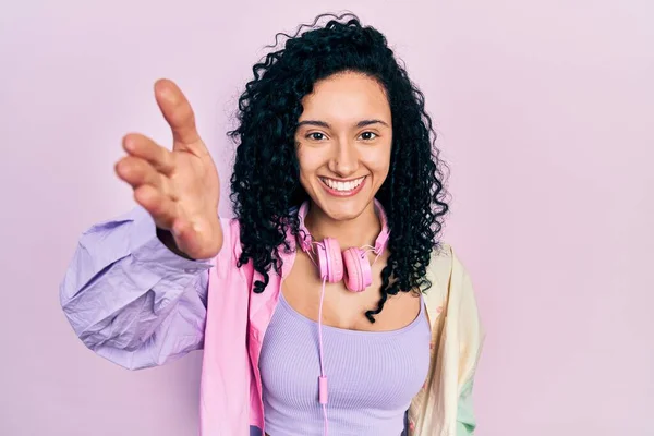 ジムの服を着て 挨拶や歓迎として握手を提供する優しい笑顔ヘッドフォンを使用して巻き毛の若いヒスパニック系の女性 成功したビジネス — ストック写真