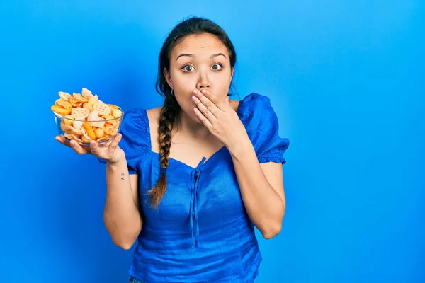 若いヒスパニック系の女の子の手で口をカバーポテトチップスのボウルを保持し ショックを受け ミスを恐れている 驚きの表情 — ストック写真