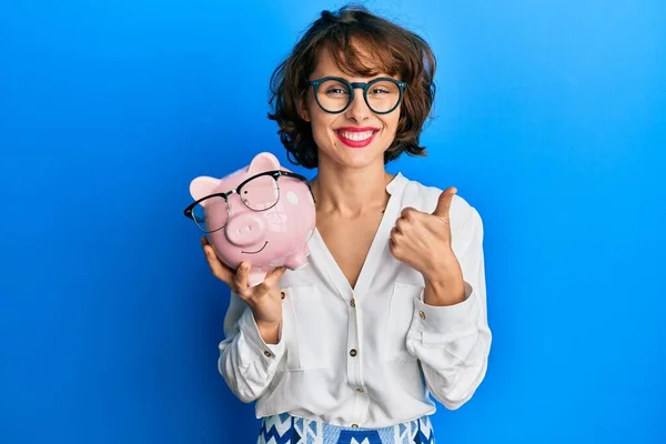 Νεαρή Μελαχρινή Γυναίκα Κρατώντας Piggy Τράπεζα Γυαλιά Χαμογελώντας Χαρούμενος Και — Φωτογραφία Αρχείου