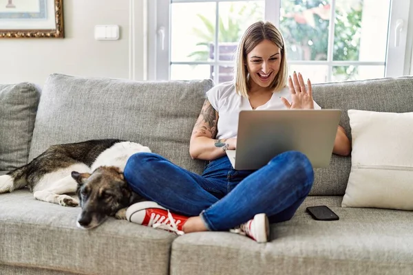 若いですCaucasian女の子座っていますオンザソファとともに犬持っていますビデオ通話を使用してラップトップホーム — ストック写真