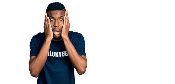 身穿志愿T恤的年轻的非洲裔美国人害怕 惊奇和惊奇 双手放在脸上 — 图库照片