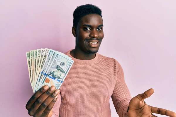 英俊的黑人男人高举双手 带着快乐的笑容和胜利的表情 拿着美元庆祝胜利 — 图库照片