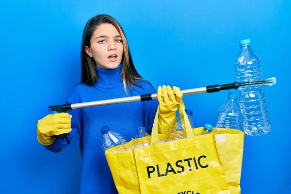 若いですブルネット女の子保持リサイクルバッグとともにプラスチックボトルと廃棄物ピッカーでショック顔 見て懐疑的かつ皮肉 驚きでオープン口 — ストック写真