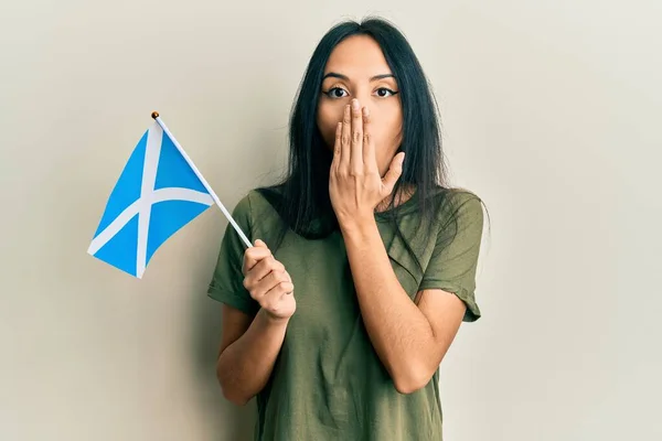 Jovencita Hispana Sosteniendo Bandera Escocia Cubriendo Boca Con Mano Conmocionada —  Fotos de Stock