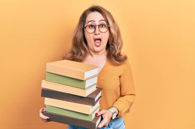 Orta yaşlı beyaz bir kadın elinde bir yığın kitap tutuyor. Şaşırmış ve şaşırmış bir ifadeyle, korku ve heyecanlı bir yüzle.. 