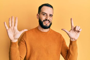 Sakallı, sıradan bir kazak giyen genç adam yedi numaralı parmaklarını gösterip gülümseyerek mutlu ve kendinden emin bir şekilde gülümsedi.. 