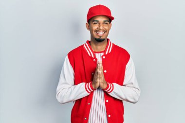 Beyzbol üniforması giyen, elleri birarada dua eden, kendinden emin gülümseyen Afro-Amerikan genç adam.. 