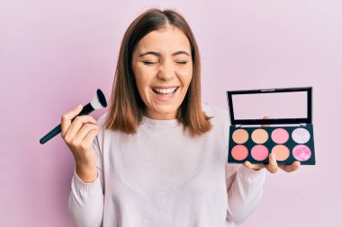 Makyaj fırçası tutan genç ve güzel bir kadın. Yüzü kızarır ve kahkahalarla güler.. 