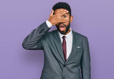 Genç Afro-Amerikan adam iş kıyafetleri içinde şok içinde yüzünü ve gözlerini kapayarak utanmış bir ifadeyle parmaklarının arasından bakıyor.. 