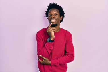 Sıradan kıyafetler giyen genç Afro-Amerikalı adam kameraya kendinden emin bakıyor kollarını kavuşturmuş ve çenesini kaldırmış gülümsüyor. Olumlu düşünmek. 