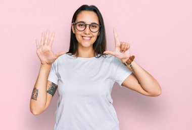 Gündelik beyaz tişört giyen genç İspanyol kadın yedi numarayı gösterip işaret ederken kendine güvenen ve mutlu bir şekilde gülümsüyor.. 