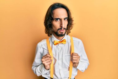 İspanyol asıllı genç adam, hippi gibi şık giyinmiş, şaşkın bakışlı, şüpheci ve alaycı görünüyor, ağzı açık kalınca şaşırıyor. 