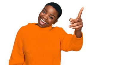 Gündelik giysiler giyen genç Afro-Amerikan kadın başarılı bir fikirle işaret ediyor. Heyecanlı ve mutlu. Bir numara.. 