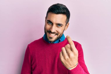 Gündelik giysiler giyen genç İspanyol adam seni buraya davet ediyor. Elinle mutlu bir şekilde karşılamaya ve gülümsemeye davet ediyor. 