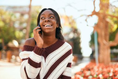 Genç Afrikalı Amerikalı kadın gülümsüyor. Parktaki akıllı telefondan konuşmaktan mutlu..