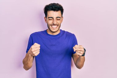 Kolları havada ve gözleri kapalı zaferi kutlayan günlük tişört giyen İspanyol genç adam. Kazanan konsept. 