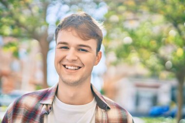 Genç beyaz adam gülümseyerek şehirde mutlu mesut duruyor..