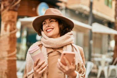 Genç İspanyol kadın akıllı telefon kullanıyor ve şehirde kahve içiyor..