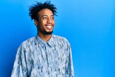 Sakallı, sıradan kıyafetler giyen, yüzünde gülümseme, doğal bir ifade olan Afro-Amerikan bir genç. Kendinden emin gülen. 