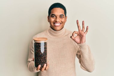 Elinde kahve çekirdekleri olan genç, yakışıklı İspanyol adam parmaklarıyla imza atıyor, gülümseyerek mükemmel bir sembol oluşturuyor. 