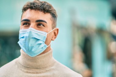 Tıbbi maske takan genç İspanyol adam şehirde dikiliyor..