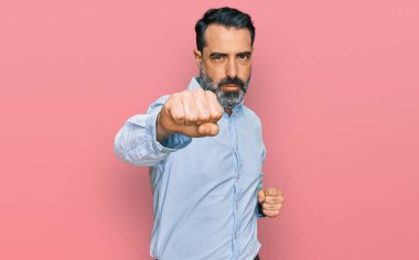 Orta yaşlı sakallı bir adam iş gömleği giyiyor. Yumruk yumruğa dövüşüyor. Agresif ve öfkeli bir saldırı. 