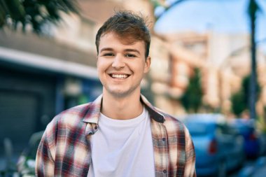 Genç beyaz adam gülümseyerek şehirde mutlu mesut duruyor..