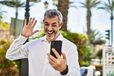 Şehirdeki akıllı telefondan video görüşmesi yapan orta yaşlı, kır saçlı bir adam..