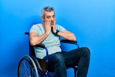 Yakışıklı, orta yaşlı, gri saçlı, tekerlekli sandalyede oturan, yorgun elleri olan, yüzü, depresyonu ve üzüntüyü örten, sorunlardan rahatsız ve rahatsız olan bir adam. 