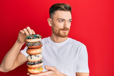 Genç kızıl saçlı adam elinde lezzetli renkli çörekler tutuyor gülümsüyor ve yan tarafa bakıyor ve düşünüyor.. 