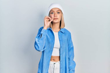 Güzel sarışın kadın yün şapkalı, ağzı ağızlı ve dudakları parmakları fermuarlı. gizli ve sessiz, tabu konuşması 