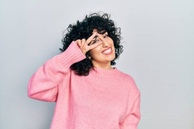 Orta Doğulu genç bir kadın günlük kıyafetler giyiyor barış sembolü yapıyor parmakları yüzünde, gülümsüyor zaferi gösteriyor. 