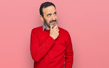 Orta yaşlı İspanyol bir adam. Elleri çenesinde gündelik giysiler giyip soru soruyor. Düşünceli bir ifade. Düşünceli bir yüzle gülümsüyor. şüphe kavramı. 