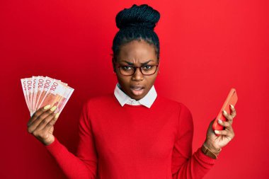 Genç Afro-Amerikalı kadın elinde Norveç Kronu banknotları olan akıllı telefon kullanıyor. Şüpheli ve alaycı görünüyor. Ağzını açtığında şaşırıyor. 