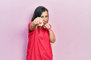 Orta yaşlı İspanyol kadın gündelik kıyafetler giyiyor dövüşmek için yumruk atıyor agresif ve öfkeli saldırı, tehdit ve şiddet 