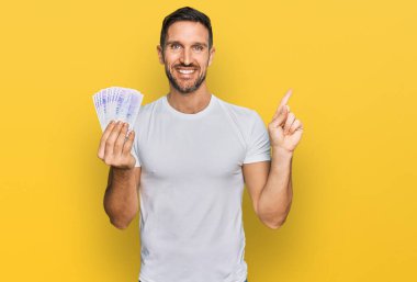 Sakallı yakışıklı adam elinde 20 İsveç banknotuyla mutlu bir şekilde gülümsüyor. 