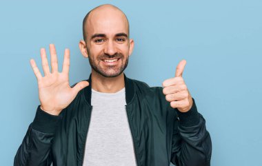 Latin asıllı genç adam gündelik giysiler giyip altı numaralı parmaklarıyla işaret ederken kendinden emin ve mutlu bir şekilde gülümsüyor.. 