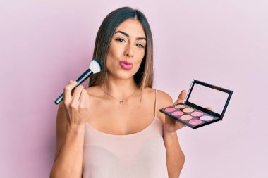 Makyaj fırçası tutan ve kameraya bakıp öpüşen sevimli ve seksi İspanyol bir kadın. aşk ifadesi. 