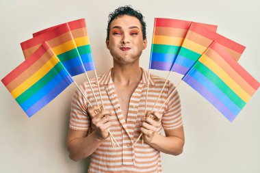 Gökkuşağı lgbtq bayraklarıyla makyaj yapan yakışıklı bir adam komik suratıyla yanaklarını şişiriyor. Ağzı havayla şişer, havayı yakalar.. 