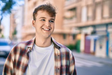 Genç beyaz adam gülümseyerek şehirde mutlu mesut duruyor..