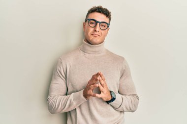 Balıkçı yaka kazak giyen İspanyol genç adam ellerini birleştirip gülümseyerek gevşemiş ve neşeli olmasını diliyordu. Başarı ve iyimserlik 